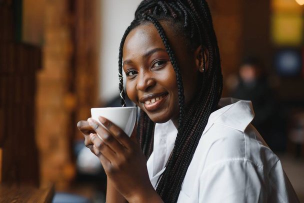 Mujer africana joven en la cafetería bebiendo café. - Foto, imagen