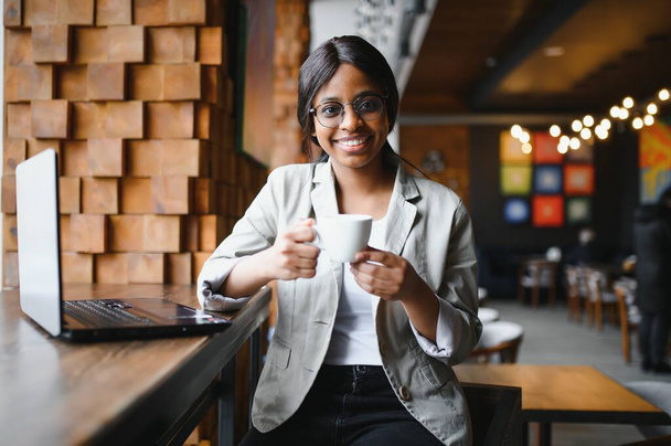 portrait of a smiling young african american woman sitting at cafe with laptop - Foto, imagen