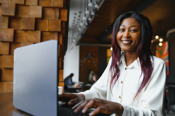 Head shot portrait of happy smiling African American woman sitting at table in cafe, looking at camera, excited female posing, working at computer, doing homework, preparing report in coffee house - Фото, зображення