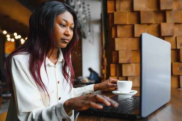 Heureuse travailleuse afro-américaine utilisant un ordinateur portable étude de travail à l'ordinateur dans le bureau loft ou un café, souriant mixte étudiante pigiste en utilisant l'application PC sortir ensemble communiquer en ligne regarder webinaire
 - Photo, image