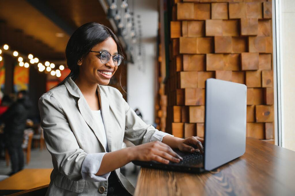 Happy african american woman worker using laptop work study at computer in loft office or cafe, smiling mixed race female student freelancer using pc app dating communicating online watching webinar - Φωτογραφία, εικόνα