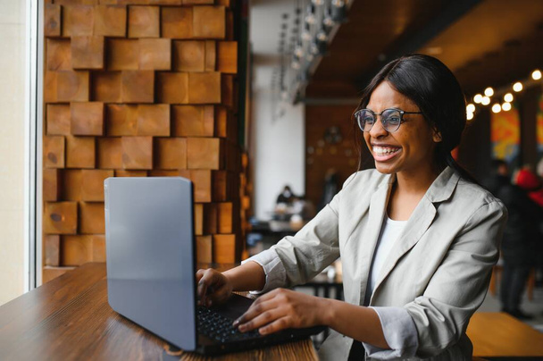 Glückstag. Emotionale schwarze Frau blickt auf Laptop, ballt Fäuste und schreit, arbeitet im Café, kopiert Raum - Foto, Bild