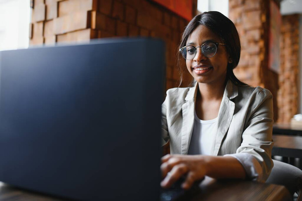 Young beautiful Afro-American businesswoman using laptop while working in cafe - Photo, image