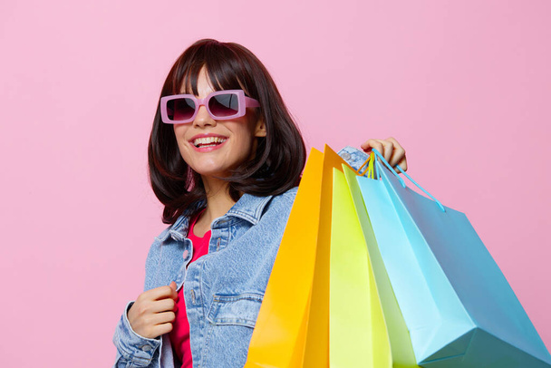 mujer joven en chaquetas de mezclilla con coloridas bolsas de compras fondo aislado - Foto, Imagen
