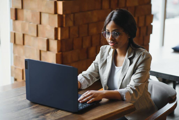 Happy african american woman worker using laptop work study at computer in loft office or cafe, smiling mixed race female student freelancer using pc app dating communicating online watching webinar - 写真・画像