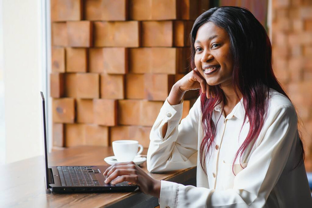 Happy african american woman worker using laptop work study at computer in loft office or cafe, smiling mixed race female student freelancer using pc app dating communicating online watching webinar - Foto, Bild