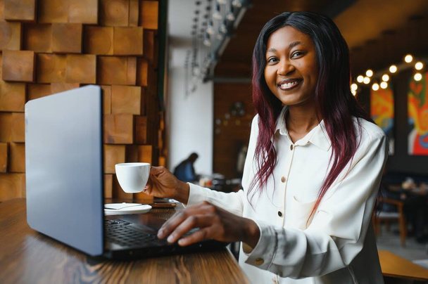 Head shot portrait of happy smiling African American woman sitting at table in cafe, looking at camera, excited female posing, working at computer, doing homework, preparing report in coffee house - Foto, Bild