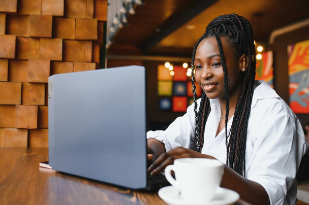 Молодая женщина сидит в кафе, пьет кофе и работает на ноутбуке - Фото, изображение