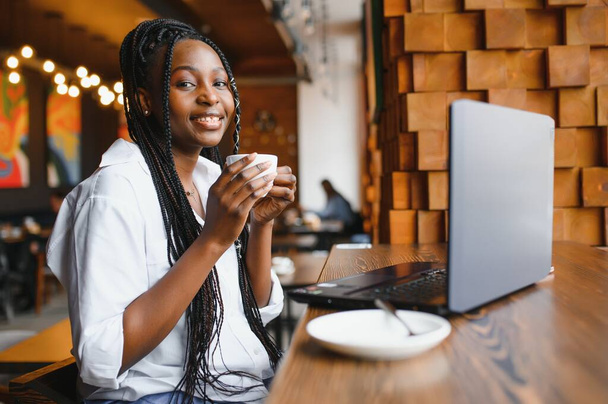 Head shot portrait of happy smiling African American woman sitting at table in cafe, looking at camera, excited female posing, working at computer, doing homework, preparing report in coffee house - Photo, Image