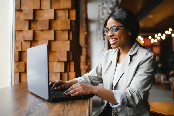 Día de suerte. Mujer negra emocional mirando a la computadora portátil, apretando puños y gritando, trabajando en la cafetería, copiando espacio - Foto, imagen