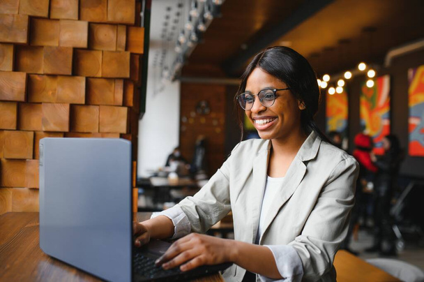 Young beautiful Afro-American businesswoman using laptop while working in cafe - Fotó, kép