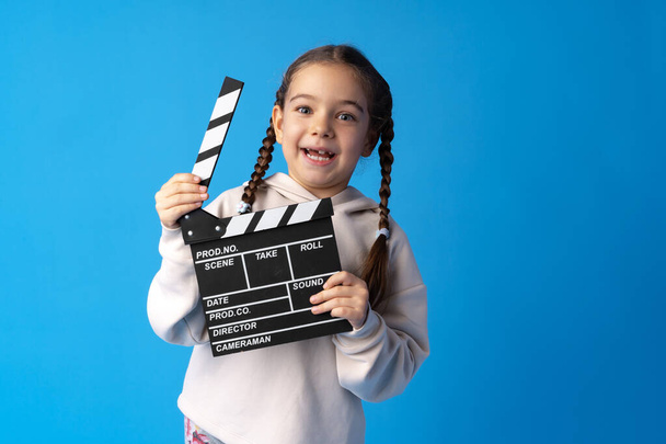 Smiling girl holding clapper board against blue background - Foto, imagen