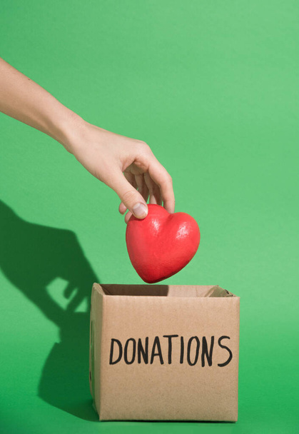 Hand placing heart in charity donations box in green background - Fotoğraf, Görsel