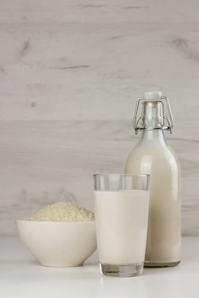 Uma garrafa e um copo com leite de arroz livre de leite alternativo e sementes em uma tigela. Bebida sem lactose - Foto, Imagem