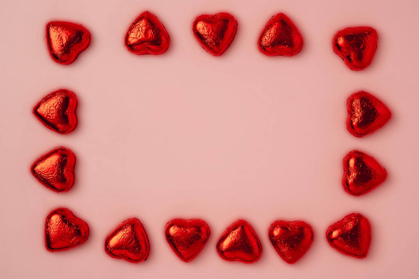 A frame of many shiny heart-shaped candies wrapped in foil on a pink background. Top view. Beautiful background for a postcard. a banner for the site. copy space - 写真・画像