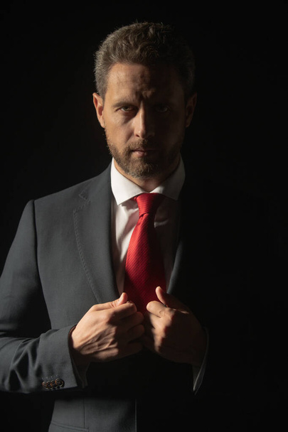 Studio portrait of serious businessman wearing suit and tie and looking thoughtfully while standing at isolated dark background. Serious business man face. - Photo, image