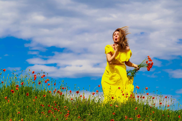 Eine Frau in einem gelben Kleid zeigt ihre Zunge auf einem Feld in der Natur. Großes Stimmungskonzept - Foto, Bild