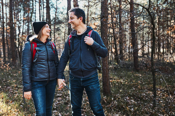 Couple holding hands enjoying trip while vacation day. Hikers with backpacks walking on forest path on sunny day. Active leisure time close to nature - Foto, afbeelding