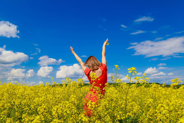 Young pretty woman in colored dress on lightning cheerful yellow background of blooming rapeseed field. Happiness concept - Foto, immagini