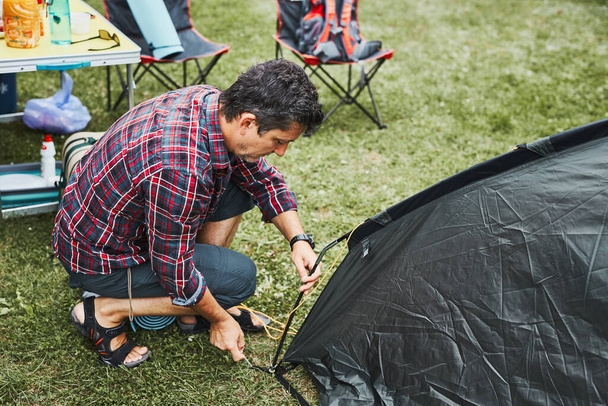 Man putting up a tent at camping during summer vacation. Preparing campsite to rest and relax. Spending vacations outdoors close to nature - Φωτογραφία, εικόνα