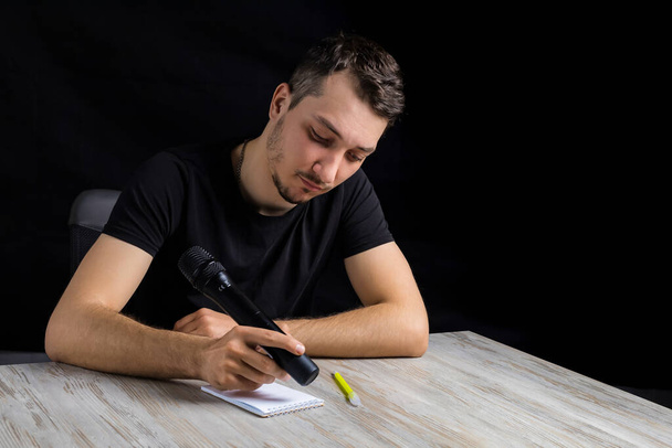 Ein junger Journalist imitiert humorvoll das Schreiben von Informationen in ein Notizbuch mit einem Stift, der statt dessen ein Mikrofon hält.. - Foto, Bild