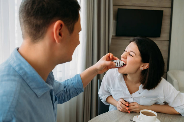 Young couple in love having fun breakfast in kitchen. Man feeds woman cake. Young people have fun in morning. Happy family. - Fotoğraf, Görsel