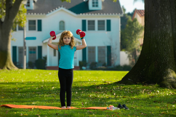 Fitness child. Sport exercise for kids. Sporty children, healthy Lifestyle. Child boy lifting dumbbells outside. - Zdjęcie, obraz