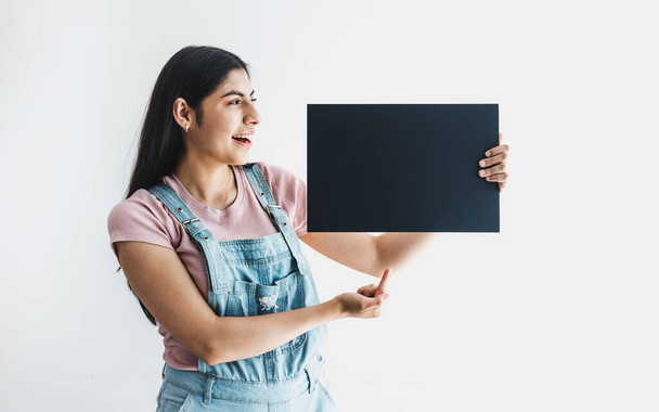young latin woman pointing at copy space in a black board or banner in Latin America - Foto, Bild