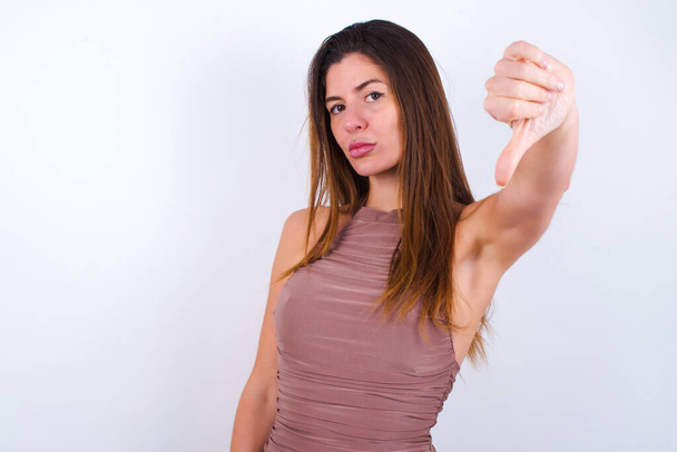 Young woman wearing sports clothing white background feeling angry, annoyed, disappointed or displeased, showing thumbs down with a serious look - Zdjęcie, obraz