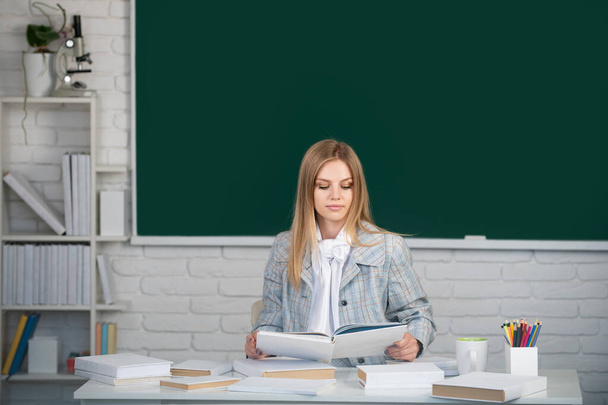 Female college student holding book in classroom, preparing for exam. Cute student girl reading book on blackboard background with copy space. - Фото, изображение