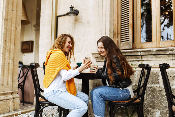 Allegro migliore amico femminile condividere file multimediali su smartphone trascorrere del tempo libero insieme, sorridente ragazze hipster bere caffè, seduto al caffè terrazza - Foto, immagini