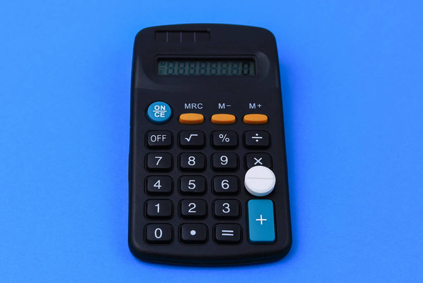 Classic medical white pill with risk mark and calculator. The concept of financial costs for the treatment of the disease. Background with copy space for text. - Fotografie, Obrázek