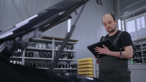 Homem mecânico no capô de um carro com um tablet diagnostica todos os sistemas e procura por avarias - Filmagem, Vídeo