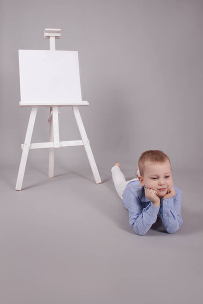 bambino in piedi vicino al cavalletto del tabellone di presentazione con set di tela bianca. Isolato su sfondo grigio. Mockup vuoto - Foto, immagini