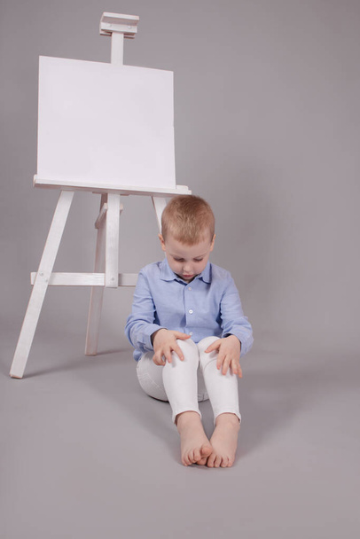 malý chlapec stojící u stojanu na prezentaci s prázdným plátnem. Izolované na šedém pozadí. Prázdná maketa - Fotografie, Obrázek