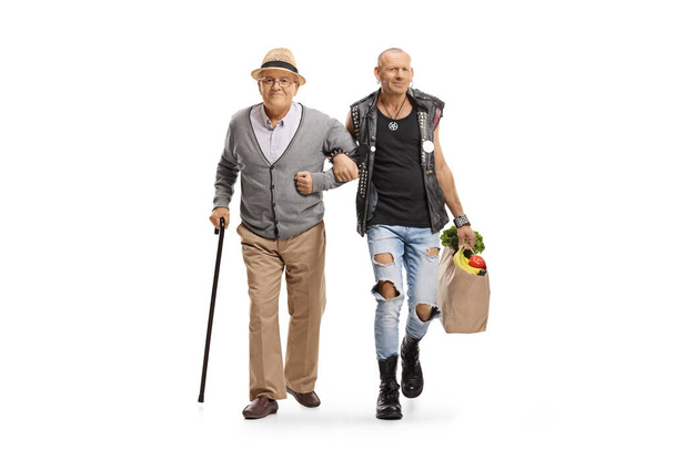 Full length portrait of a punk helping an elderly man with a cane and carrying grocery bags isolated on white background - Foto, afbeelding