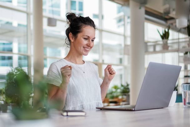 happy smiling  successful remote working dark haired woman cheerful infront of laptop or notebook in casual outfit sitting on work desk in her modern loft living room home office having a video chat - Foto, immagini