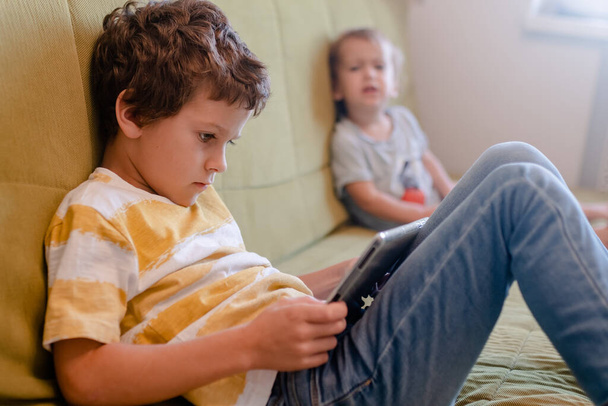 chico en amarillo y blanco camiseta con entusiasmo juega un juego en una tableta - Foto, Imagen