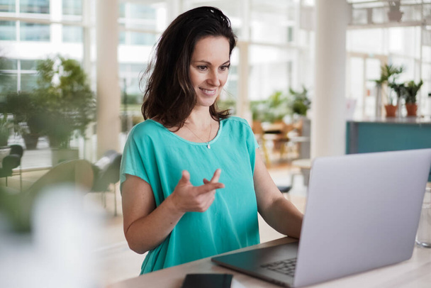 happy smiling  successful remote working dark haired woman cheerful infront of laptop or notebook in casual outfit sitting on work desk in her modern loft living room home office having a video chat - Foto, immagini