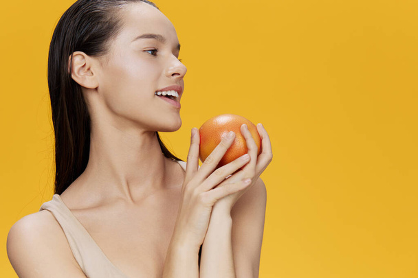 brunette  with grapefruit in hands posing on  yellow background. High quality photo - Foto, afbeelding