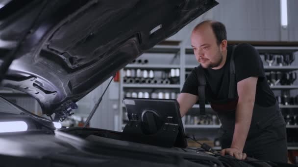 Man monteur op de motorkap van een auto met een tablet diagnosticeert alle systemen en zoekt naar storingen - Video