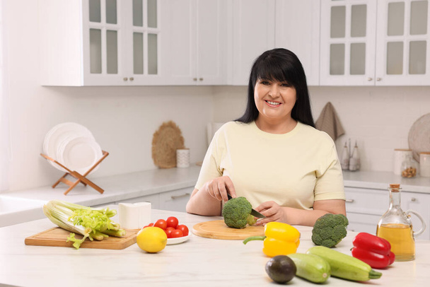 Gyönyörű túlsúlyos nő, aki egészséges ételt készít az asztalnál a konyhában - Fotó, kép