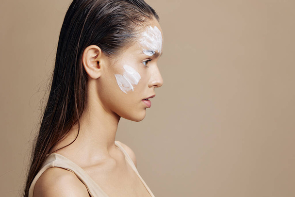 mujer con crema hidratante en las mejillas sobre fondo beige. Foto de alta calidad - Foto, Imagen