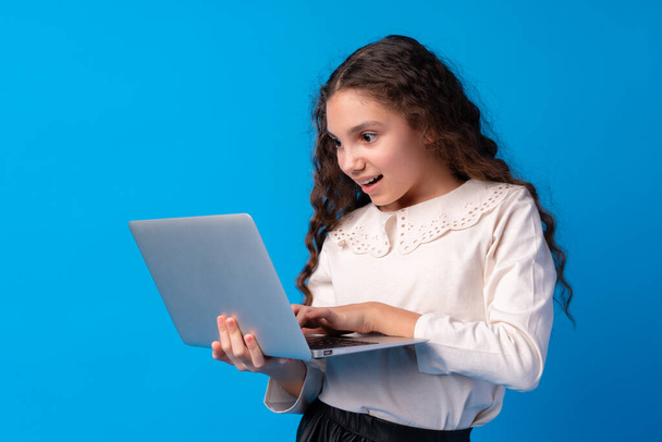 Portrait of a little girl holding laptop computer while standing against blue background - Fotó, kép