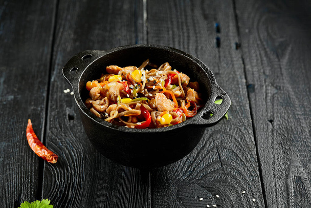 Yakisoba noodle with chicken and vegetables on wooden background. Japanese stir fry noodles in wok on black table with ingredients. Chicken with buckwheat soba on wok. Oriental cuisine. Wok menu - 写真・画像