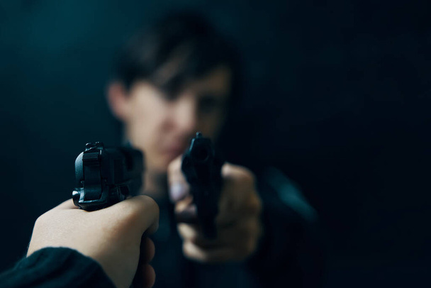 Κοντινό πλάνο των ανδρών χέρι με το όπλο στραμμένο σε εγκληματία με περίστροφο. - Φωτογραφία, εικόνα