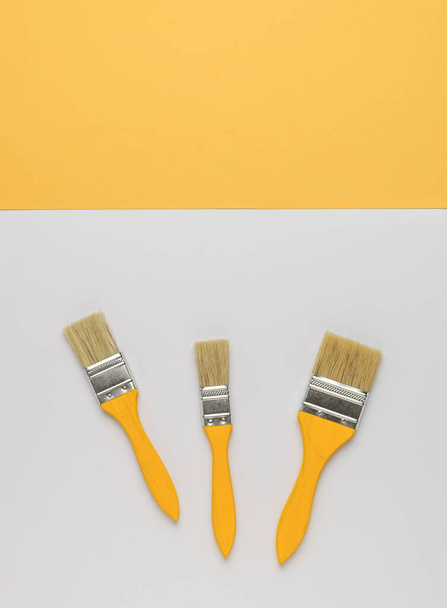 Three paint brushes on a white background and a yellow stripe. Trending color. Flat lay. - Fotoğraf, Görsel