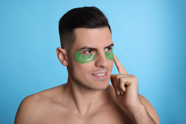 Man applying green under eye patch on light blue background - Photo, Image