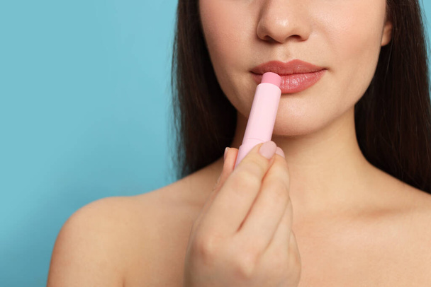 Young woman applying lip balm on turquoise background, closeup. Space for text - Photo, Image