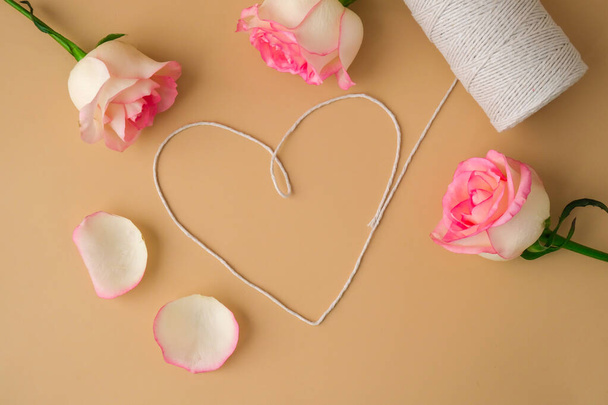 Tender pink roses with spool of white cotton rope in heart shape on beige background. Minimal trendy composition. Neutral earth tones. Greeting card for Valentines Mothers Womens day - Fotografie, Obrázek